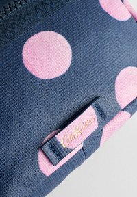 Jūras flotē un rozā svītrota auduma maisiņš ar teksturētu virsmu. Iespējojot rāvējslēdzēju un ar zīmolu apzīmējumu.