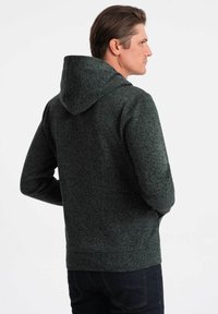 Felpa con cappuccio grigio antracite in maglia strutturata, dotata di tasca a marsupio e polsini a costine, vista da dietro, indossata da un modello.