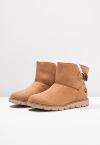 Bottines en daim camel avec doublure en fausse fourrure blanche, bouts ronds, sangle avec boucle décorative sur le côté et semelles en caoutchouc texturé.