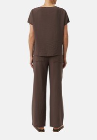 Bruine, lichtgewicht, gestructureerde top gecombineerd met bijpassende broek met wijde pijpen. Eenvoudig ontwerp, korte mouwen, achterzakken op de broek.