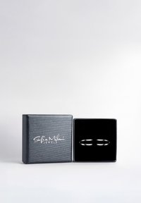 Des bagues en métal argenté exposées dans une boîte tapissée de velours noir, avec un extérieur gris texturé et un texte logo blanc sur le couvercle.