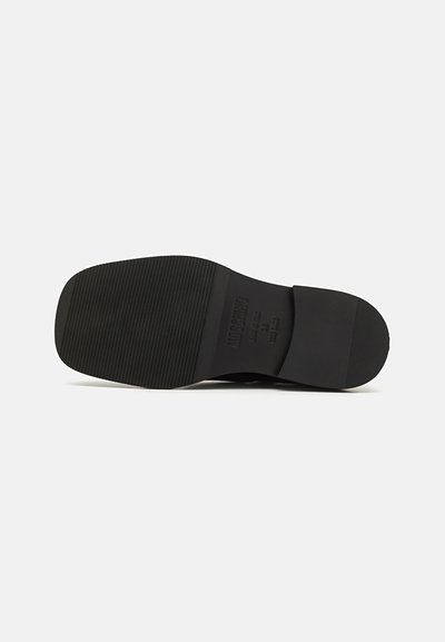 Black shoe sole with a textured, ribbed pattern and a smooth heel. Stamped branding details are visible near the heel area.