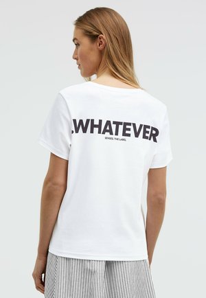 Woman with long blonde hair, seen from behind, wears a white T-shirt with “WHATEVER” in bold black text and a striped skirt.