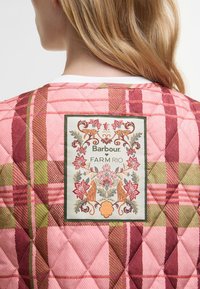 Tecido acolchoado em padrões quadriculados rosa, verde e burgundy, com um patch decorativo central que apresenta designs florais e de animais, rotulado "Barbour FARM Rio."
