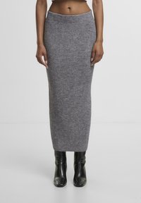 Grauer Strick-Midi-Rock mit vertikalen Rippungen, elastischem Bund und taillierter Silhouette. Kombiniert mit schwarzen, hohen Stiefeletten.