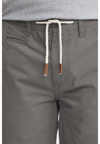 Shorts en coton gris avec une taille élastique à cordon, ornés d'un accent en cuir beige sur les extrémités du cordon et d'une poche latérale.