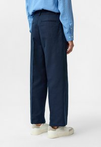 Navyblauwe wijde broek gemaakt van een gladde stof, met een ritszak en achterzakken, gecombineerd met witte sneakers.