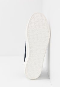 Marineblaue Sneaker mit einer strukturierten weißen Gummisohle. Die Sohle verfügt über eingeprägte Markenbeschriftungen und ein glattes Obermaterial.