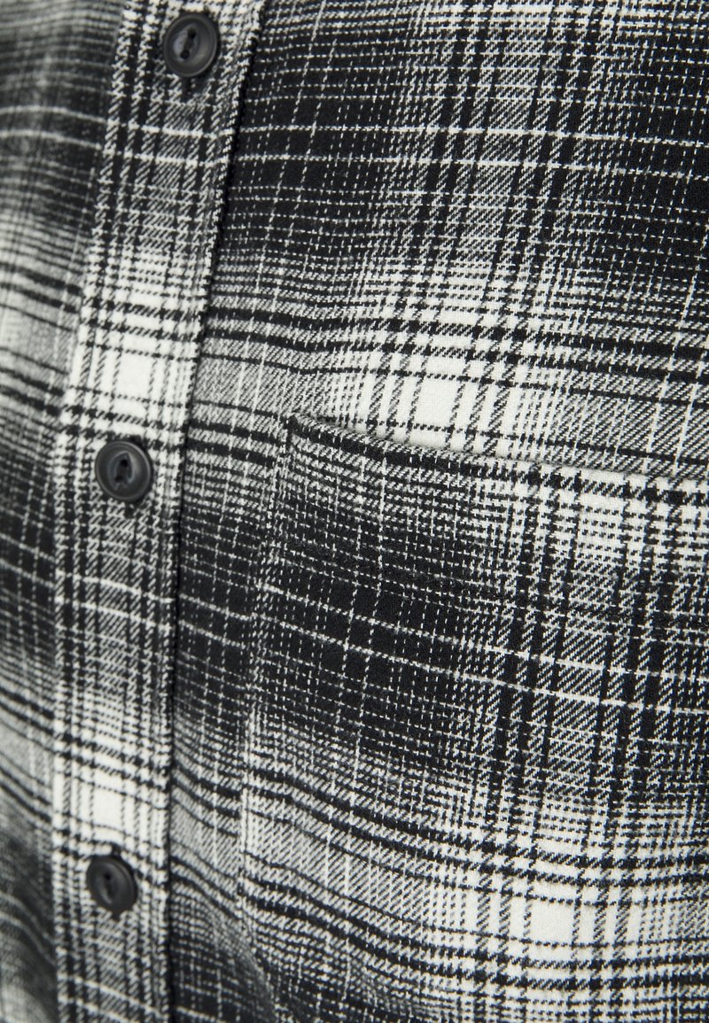 Tissu de chemise à carreaux noir et blanc avec des boutons noirs et une petite poche sur la poitrine.