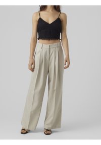 Mustat virkattu crop-top, jossa on ohuet hihnat; beige leveälahkeiset housut, joissa on laskokset; mustat litteät sandaalit. Neutraalit sävyt ja teksturoitu kangas.