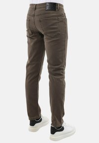 Bruine slim-fit jeans met een gladde textuur, voorzien van achterzakken en een merkband, gecombineerd met witte sneakers.