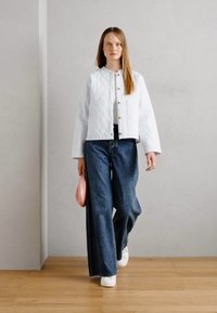 Veste matelassée blanche avec un col rond et une fermeture à boutons, associée à un jean bleu à jambes larges et des baskets blanches. Accessoire de pochette rose.