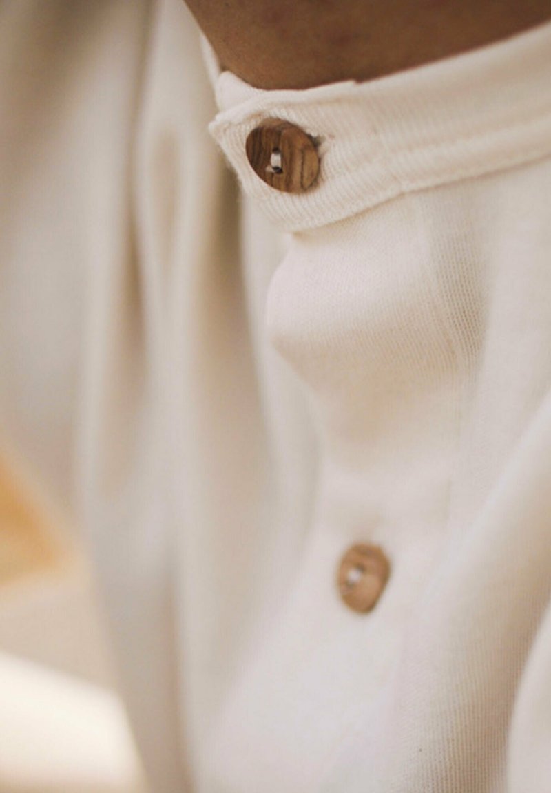 Hellebeige kragenlose Bluse mit einem Holzknopfdetail am Hals, aus einem weichen Baumwollmix mit glatter Textur.