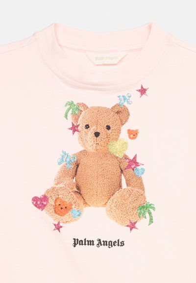 Lichtroze shirt met een getextureerde teddybeer omringd door kleurrijke sterren, harten, palmbomen en de tekst "Palm Angels" eronder.