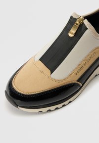 Sneaker slip-on beige e nera con cerniera dorata e logo "MARCO TOZZI" sul lato, che combina materiali in suede, tessuto e pelle verniciata.