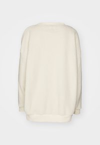 Kremowy, oversize sweter z polaru o miękkiej teksturze, okrągłym dekolcie, opuszczonych ramionach i ściągaczu na dole. Gładki tył bez dodatków.