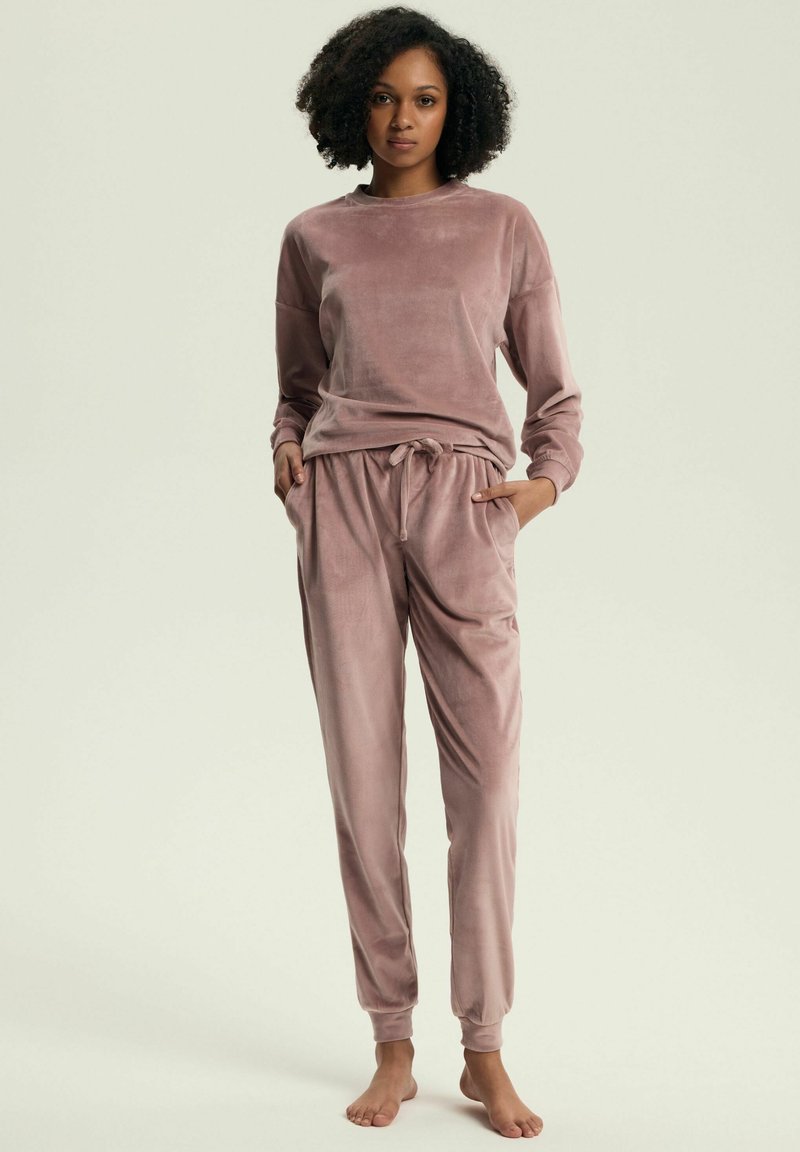 Welwetowy zestaw odzieży domowej w miękkim różowym kolorze, zawierający bluzę z długim rękawem oraz spodnie z elastycznym paskiem i kieszeniami. Gładka tekstura i luźny krój.