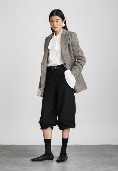 Blazer s uzorkom houndstooth, bijela bluzica s mašnom, crne culottes hlače, crne balerinke, uparen s prozirnim crnim čarapama. Neutralna pozadina, minimalistički stil.