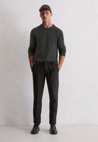 Sweter w ciemnoszarym kolorze, teksturowany materiał; czarne spodnie plisowane; czarne buty; szara czapka. Prosty krój z prążkowanymi mankietami, minimalistyczny design.