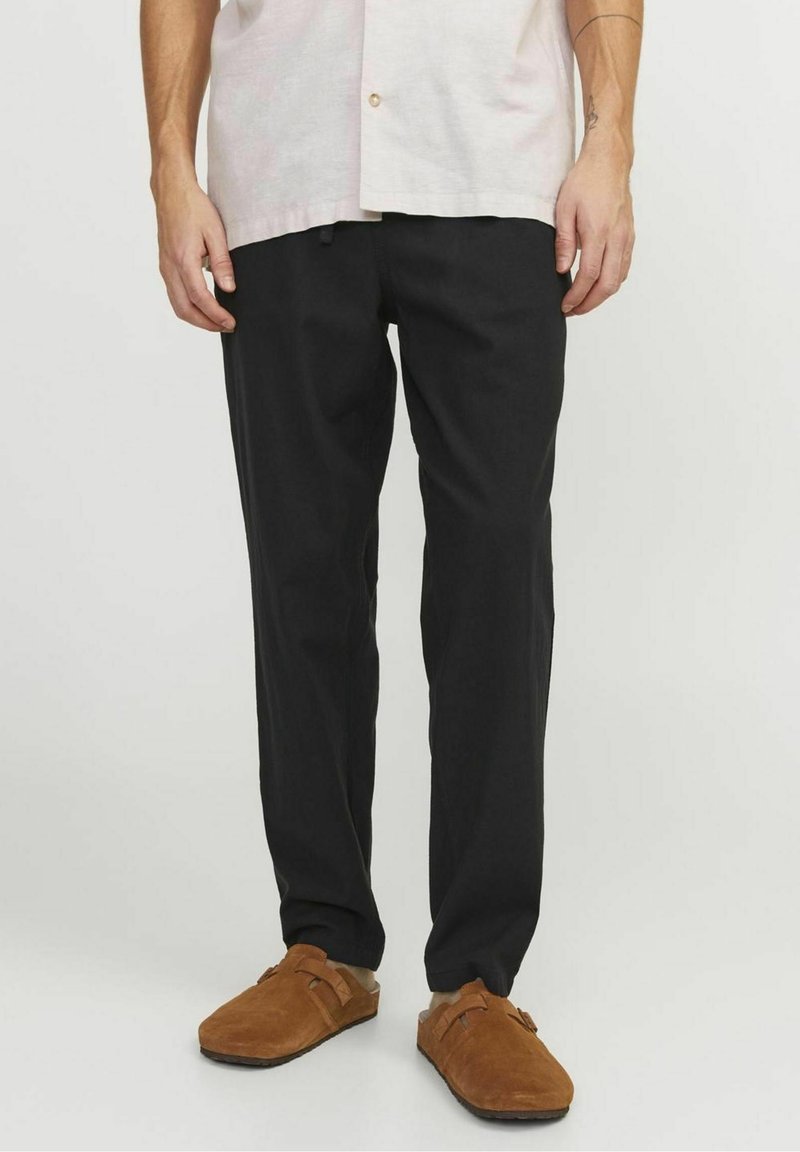 Pantalon noir en tissu doux, avec une coupe décontractée. Associé à des sabots en daim marron et une chemise légère à manches courtes.