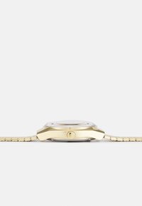 Montre en or avec un boîtier rond, un verre en façade et un bracelet en métal texturé. Présente une couronne sur le côté et un cadran réfléchissant.