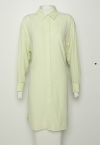 Longue robe-chemise jaune pâle à boutons, manches longues et col pointu sur un mannequin sur fond blanc.