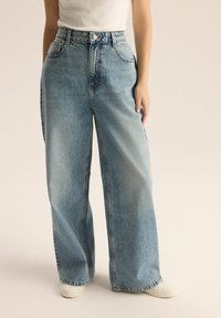 Jasnoniebieskie dżinsy o szerokich nogawkach, wykonane z denimu, z wysokim stanem, przednimi kieszeniami oraz zamkiem z zapięciem na guzik. Gładka faktura.