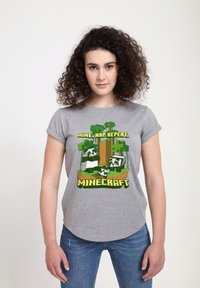 Szara koszulka z krótkim rękawem z kolorową grafiką "Minecraft" przedstawiającą drzewa i postacie, wydrukowaną w zielonym i żółtym kolorze.