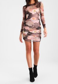 Květinové šaty s dlouhým rukávem a přiléhavým střihem, z průsvitného materiálu, s nabíranými detaily a vzorem růžových, bílých a zelených květin na tmavém pozadí.