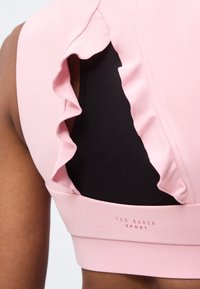 Πίσω όψη ροζ αθλητικού σουτιέν με βολάν στις άκρες πάνω από μαύρο υποστρώμα στον ώμο και το άνω μέρος της πλάτης ενός ατόμου.