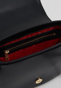 Černá kožená kabelka s hladkou texturou, s červeným vnitřkem s logovým vzorem a kapsou na zip se zlatým zipem.