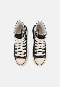 Vysoké tenisky z černé plátěné látky s bílými tkaničkami, béžovým gumovým špičkovým krytem a strukturovanou podrážkou. Mají jemné květinové akcenty po stranách.