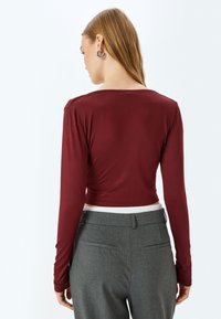 Bordeaux lange mouwen crop top met een gladde textuur, gecombineerd met grijze hoge taillebroeken met een klassiek ontwerp en achterzakken.