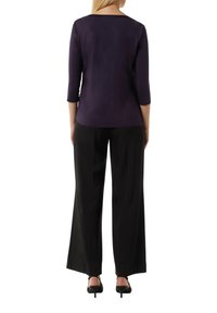 Lila Oberteil mit drei Viertelärmel, kombiniert mit schwarzen weiten Hosen. Glatte Textur; minimalistisches Design mit Rundhalsausschnitt.