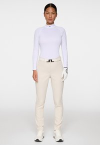 Pitkähihaista valkoista urheilu paitaa, kermaisia housuja, valkoista golfkäsilä mittausta, ja valkoisia tennareita mustilla yksityiskohdilla. Sileä kangas ja istuva muotoilu.