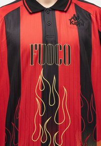 Κόκκινο και μαύρο ριγέ πόλο με σχέδιο κίτρινες φλόγες και το κείμενο «FUOCO», με το λογότυπο της Kappa στο στήθος.