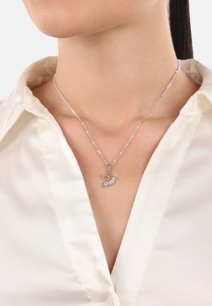 Collar de plata con un colgante de ave, detalle intrincado, sobre una cadena delgada, usado sobre una camisa blanca con cuello.