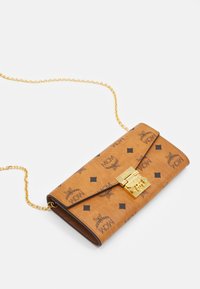 Billetera de cuero marrón con cadena dorada, que presenta un cierre de solapa, logotipos en relieve y patrones de diamantes negros en todo su diseño.