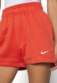 Punaiset puuvillaiset urheilushortsit, joissa on joustava vyötärö ja valkoinen Nike-logo vasemmassa alakulmassa. Pehmeä kangas ja rento malli.