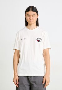 Weißes Baumwoll-T-Shirt mit kurzen Ärmeln, das auf der linken Brust ein kleines gesticktes "Champion"-Logo in Rot und Blau zeigt.