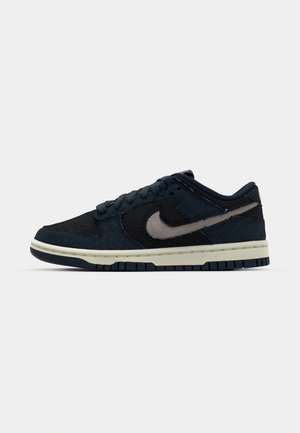 Nike Dunk Low sneaker sötét tengerészkék és fekete textúrákban, kiemelkedő világosszürke swoosh-sal, sima talppal és párnázott gallérral.