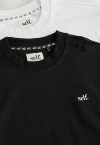 To sweatshirt i sort og hvid. Hver af dem har en ribbet halsudskæring og en lille broderet "self." logo på brystet og halsudskæringen.
