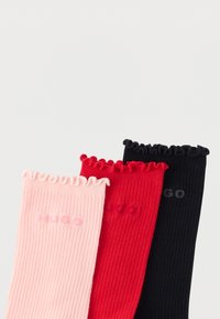 Kolm paari soonikkoes sokke roosas, punases ja mustas värvitoonis, millel on kortsulised ülemised servad ja "HUGO" brändi nimi vastavates värvitoonides.