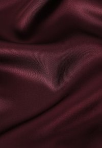 Țesătură de satin burgund cu o textură netedă și lucioasă și o cădere subtilă, arătând pliuri moi și reflexii de lumină pe suprafață.