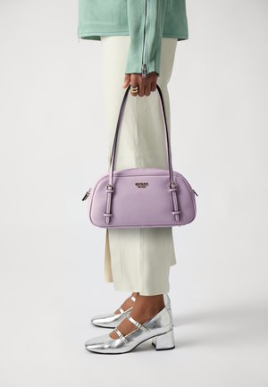 Borsa a tracolla viola con texture liscia, doppio manico superiore e dettagli argentati. Indossata con pantaloni chiari e scarpe argentate lucide.