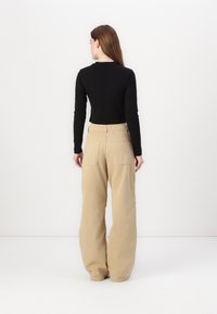 Maglietta nera a maniche lunghe con una vestibilità cropped abbinata a pantaloni beige a gamba larga con due tasche posteriori e un tessuto testurizzato.
