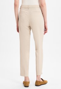 Beige tailor-made broeken van textuurstof, slim fit, twee achterzakken en een enkellange zoom, gecombineerd met bruine suède loafers.