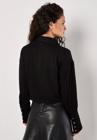 Czarna koszula z długim rękawem z kołnierzykiem, z guzikami na mankietach i skróconym fasonem, wykonana z gładkiego, miękkiego materiału.