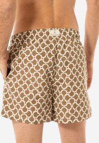 Costume da bagno marrone con un motivo geometrico ripetuto in crema e rosso. Vita elastica con etichetta sul retro. Tessuto leggero.
