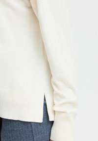 Krämfärgad stickad tröja med avslappnad passform, med sidofrackar, ribbade ärmslut och en mjuk textur. Matchas med texturerade mörkblå byxor.